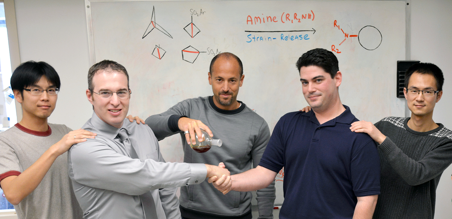 Chemists from The Scripps Research Institute illustrate their powerful new technique to make and modify medicines, published recently in the journal Science. Professor Phil Baran (center) holds a flask representing amines to cleave strained C–C bonds, which are depicted by a tug-of-war between co-first authors Ryan Gianatassio (left center) and Justin Lopchuk (right center) with co-authors Chung-Mao Pan (left)  and Jie Wang.